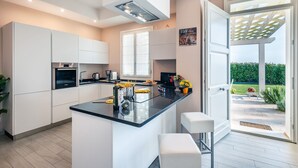 A modern kitchen with a central island, white cabinetry, and a view to a garden through a glass door. - Stunning private villa for 13 people with A/C, private pool, WIFI, hot tub, sauna, TV and patio (Cintolese)