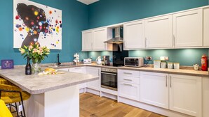 A modern kitchen with white cabinets, a central island, and a teal accent wall. - The School House - sleeps 2 guests  in 1 bedroom (York)