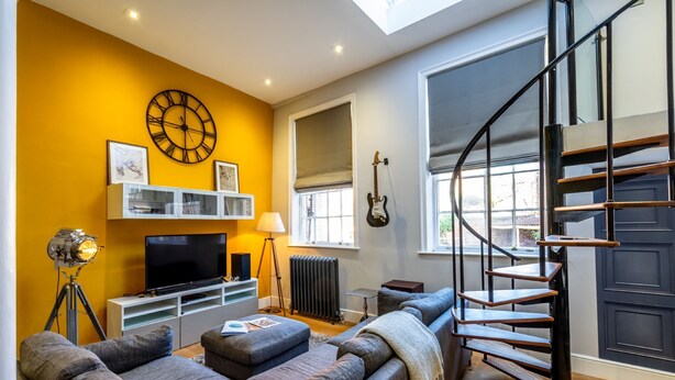 A living room with a sofa, a TV, a clock, and a staircase. - The School House - sleeps 2 guests  in 1 bedroom (York)