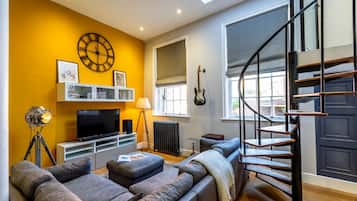A living room with a sofa, a TV, a clock, and a staircase.