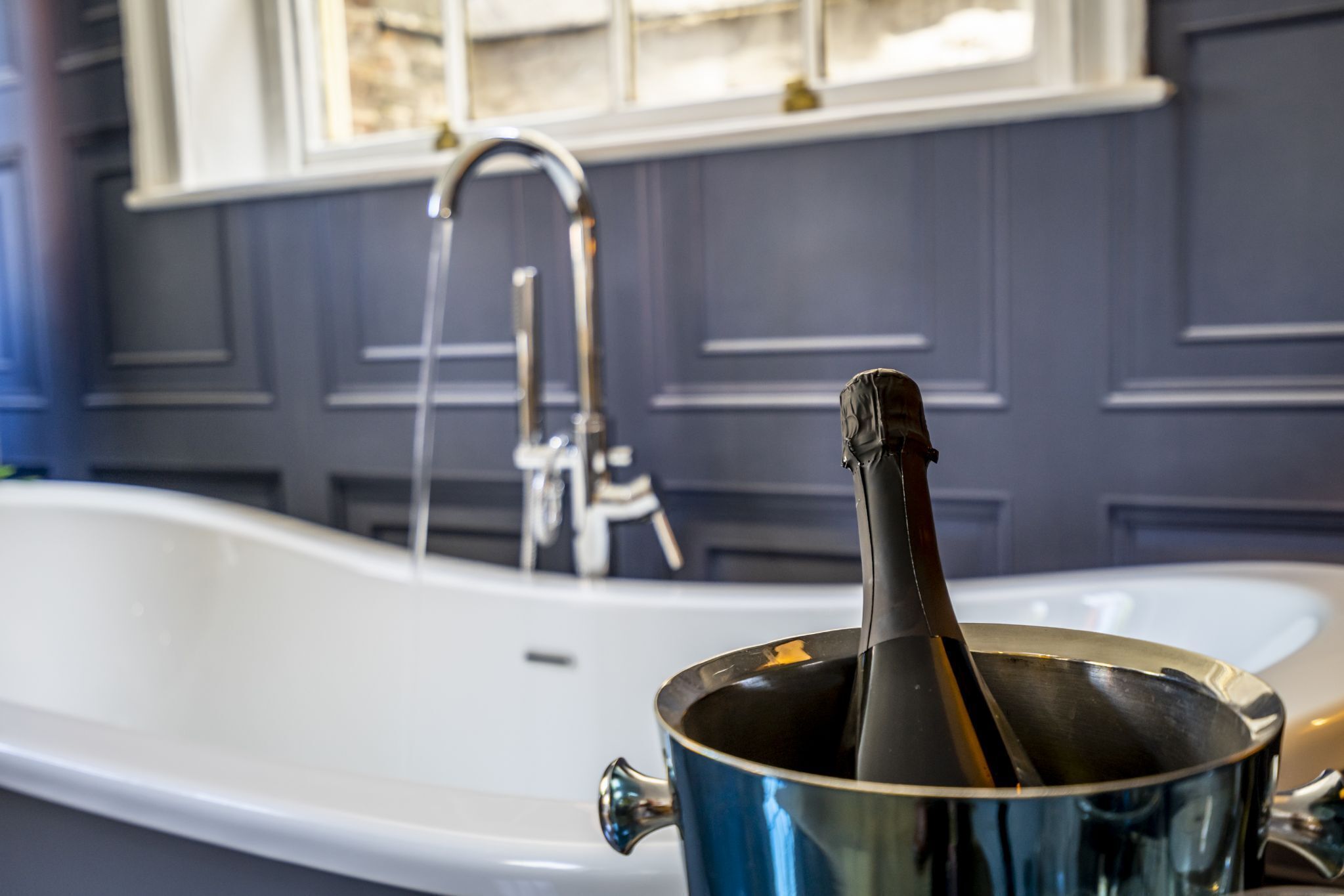 A bathtub with a faucet and a bottle of champagne in a bucket.