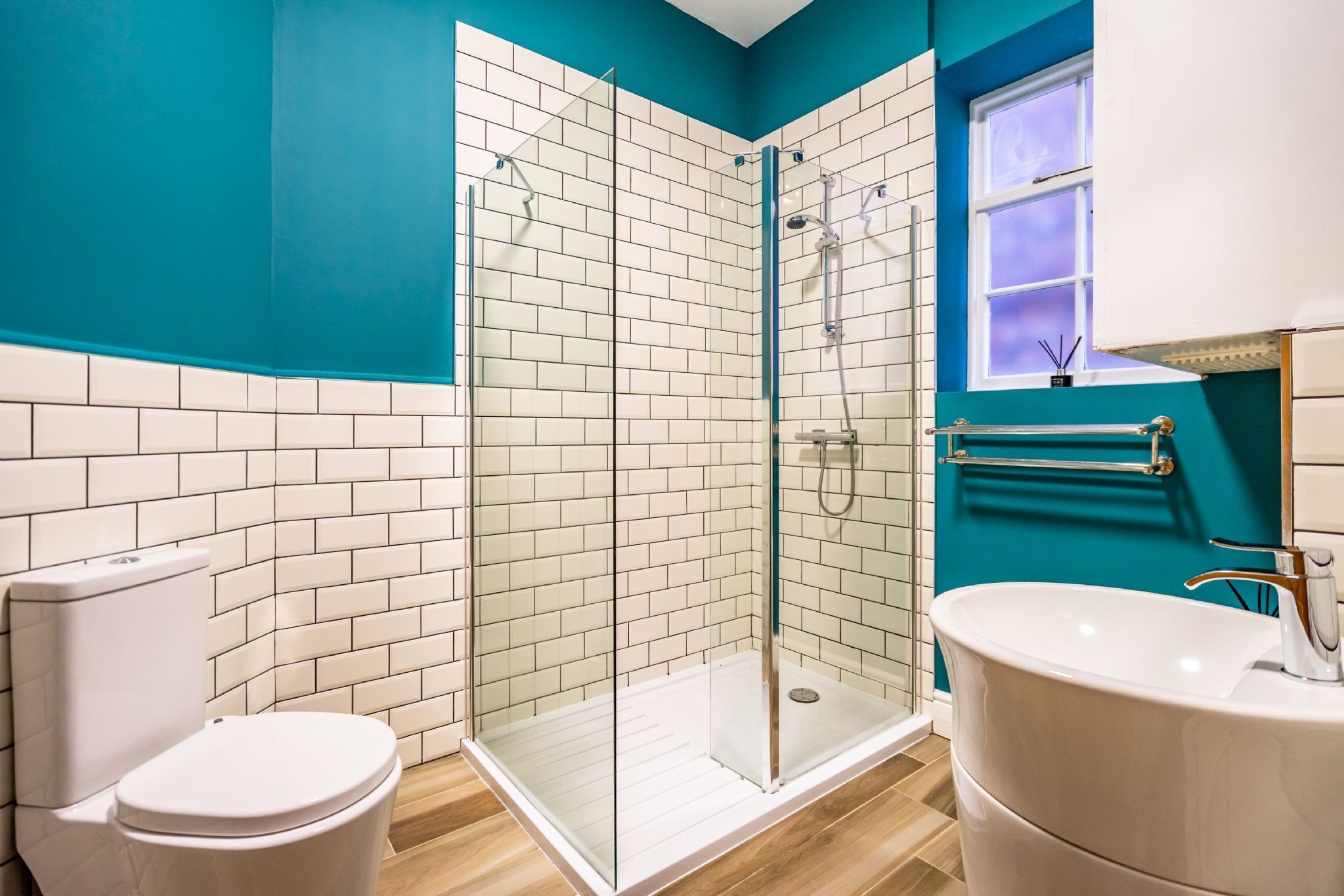 A modern bathroom with a glass-enclosed shower, white tiles, and a teal accent wall.