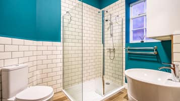 A modern bathroom with a glass-enclosed shower, white tiles, and a teal accent wall.