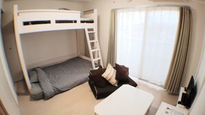 Een kleine kamer met stapelbedden, een bureau en een raam met gordijnen.