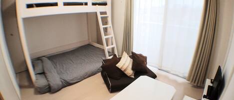 A compact room with bunk beds, a small desk, and a window with curtains.