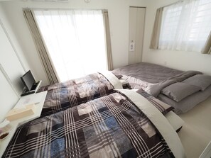 Un dormitorio con dos camas, un escritorio con una computadora portátil y una ventana con cortinas.