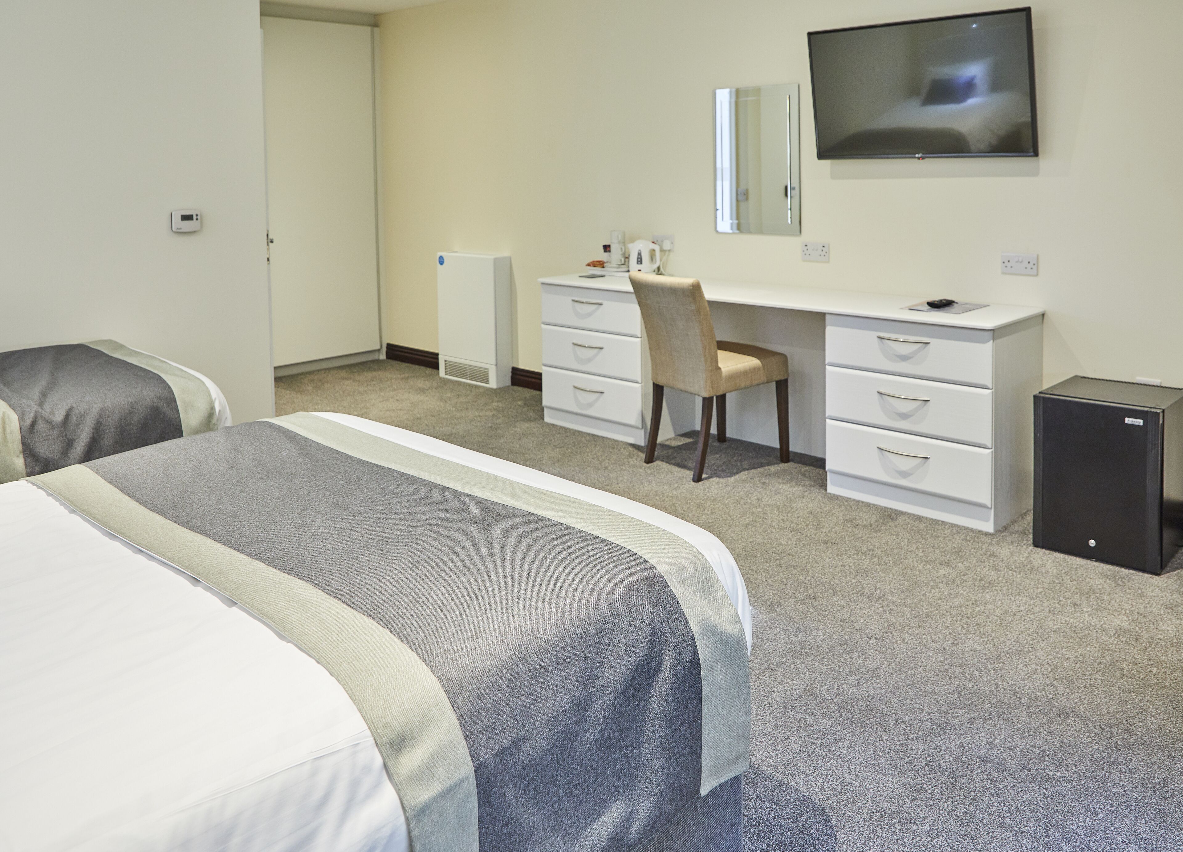 Une chambre d’hôtel avec deux lits, un bureau avec une chaise, une télévision et une petite enceinte noire.