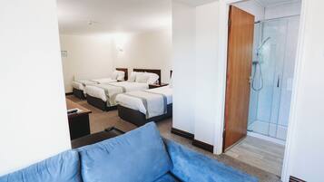 A hotel room with two beds, a shower, and a blue sofa.