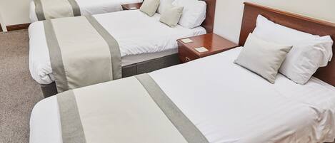 Une chambre d’hôtel avec deux lits simples, chacun doté d’une tête de lit en bois, de draps blancs et d’une bande décorative grise. Une table de chevet en bois se trouve entre les lits, et un radiateur est fixé au mur.