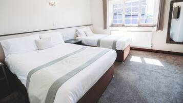 A hotel room with two beds, a window with curtains, a wall-mounted TV, and a radiator.
