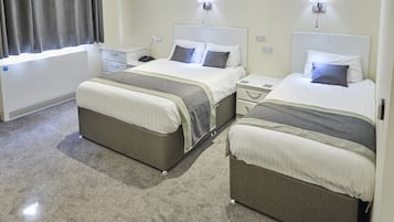 A hotel room with two beds, a bedside table, a nightstand, and a window with curtains.