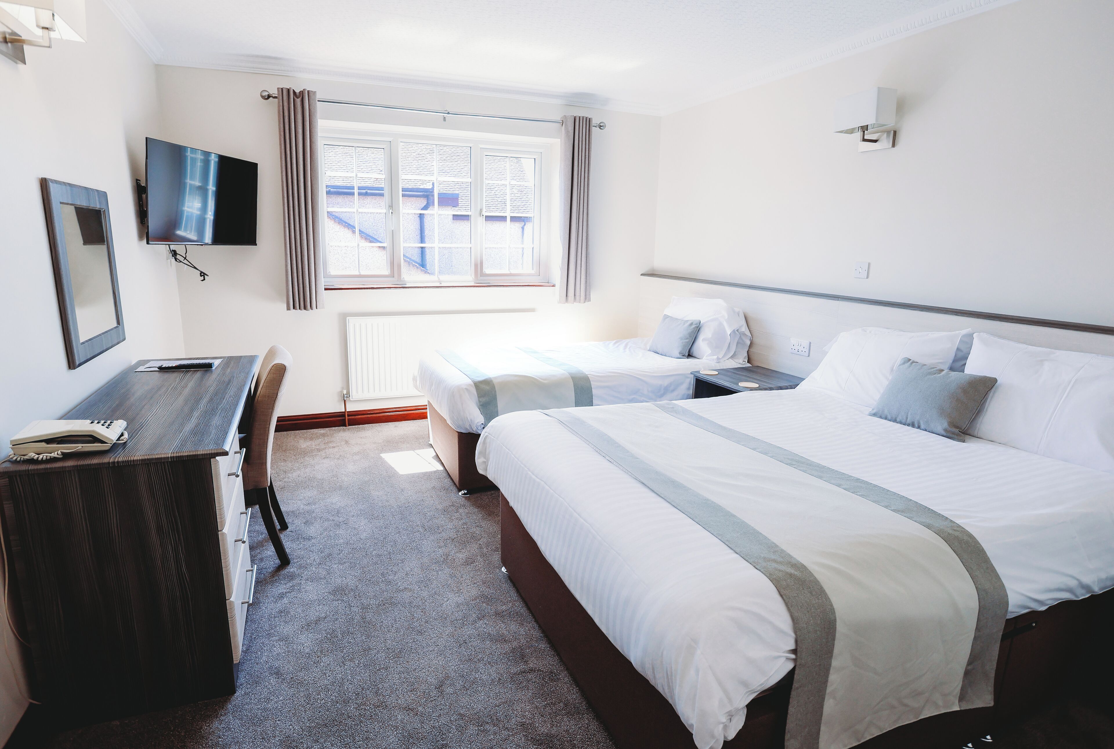 Habitación de hotel con cama, escritorio, silla, televisor y ventana con cortinas.