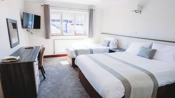 Habitación de hotel con cama, escritorio, silla, televisor y ventana con cortinas.