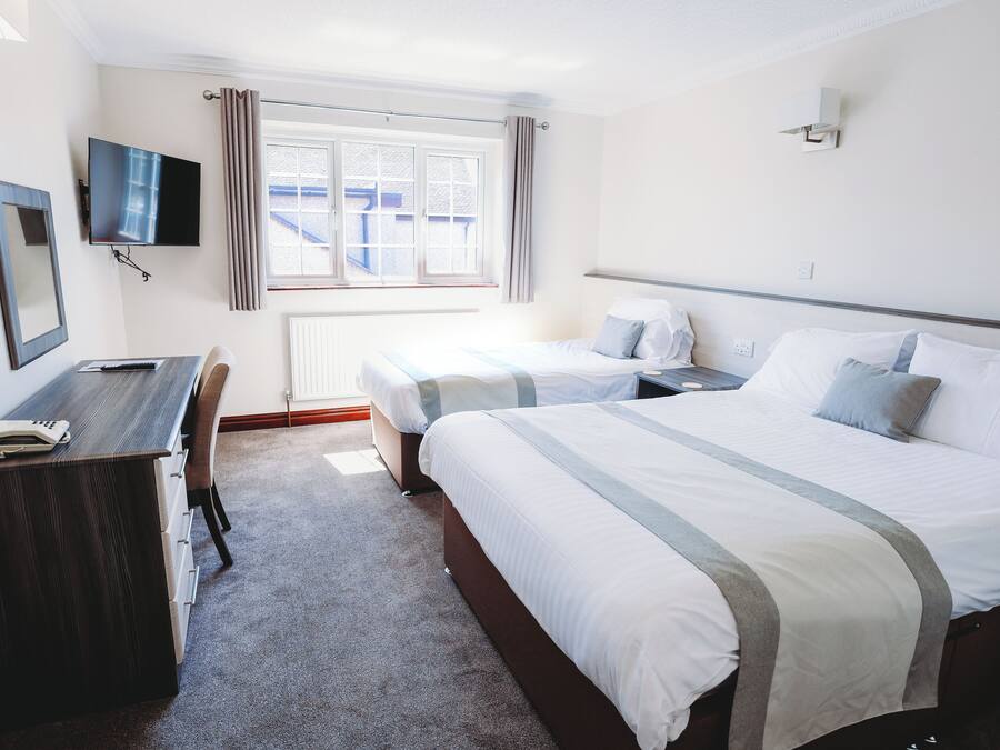 Habitación de hotel con cama, escritorio, silla, televisor y ventana con cortinas.