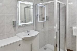 A modern bathroom with a glass-enclosed shower, a white sink, and a large mirror. - Appleby Inn Hotel (Swadlincote)
