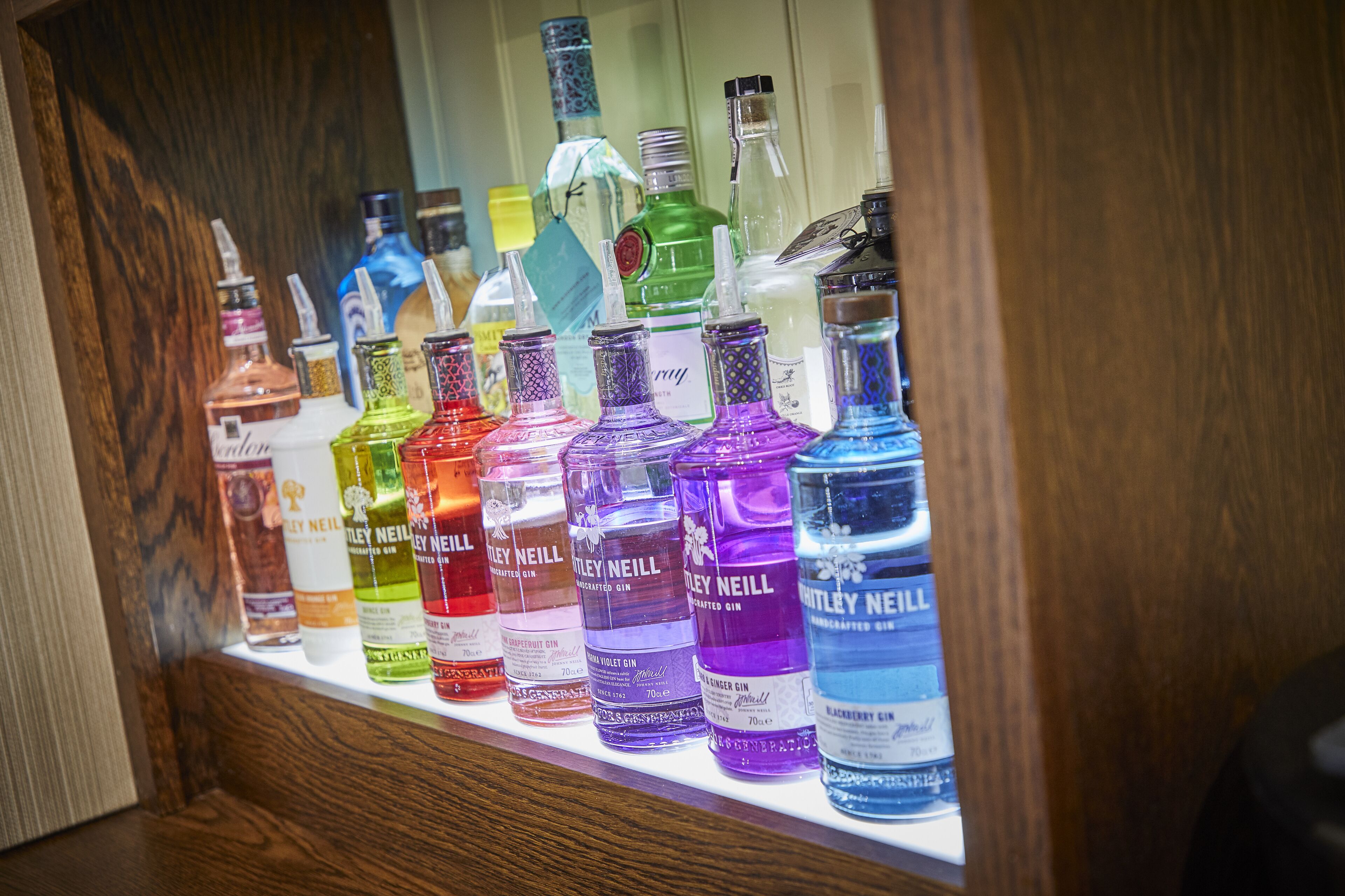 Diverse flessen Bailey Neill gin in een houten kast.