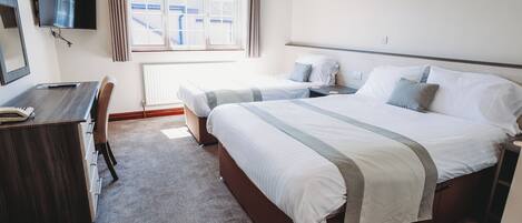 A hotel room with a bed, a desk, a chair, a TV, and a window with curtains.