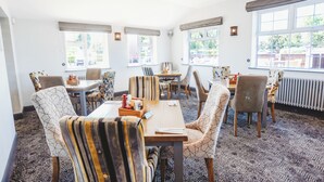 A dining area with striped chairs, a wooden table, and large windows. - Appleby Inn Hotel (Swadlincote)