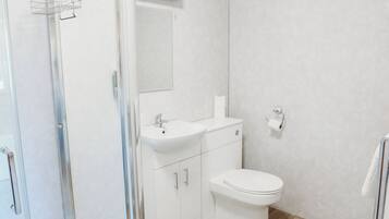 Un baño moderno con cabina de ducha de vidrio, un lavabo blanco y un inodoro.