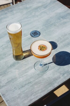 A table with a tall glass of beer and a cocktail with a fruit garnish. - Appleby Inn Hotel (Swadlincote)