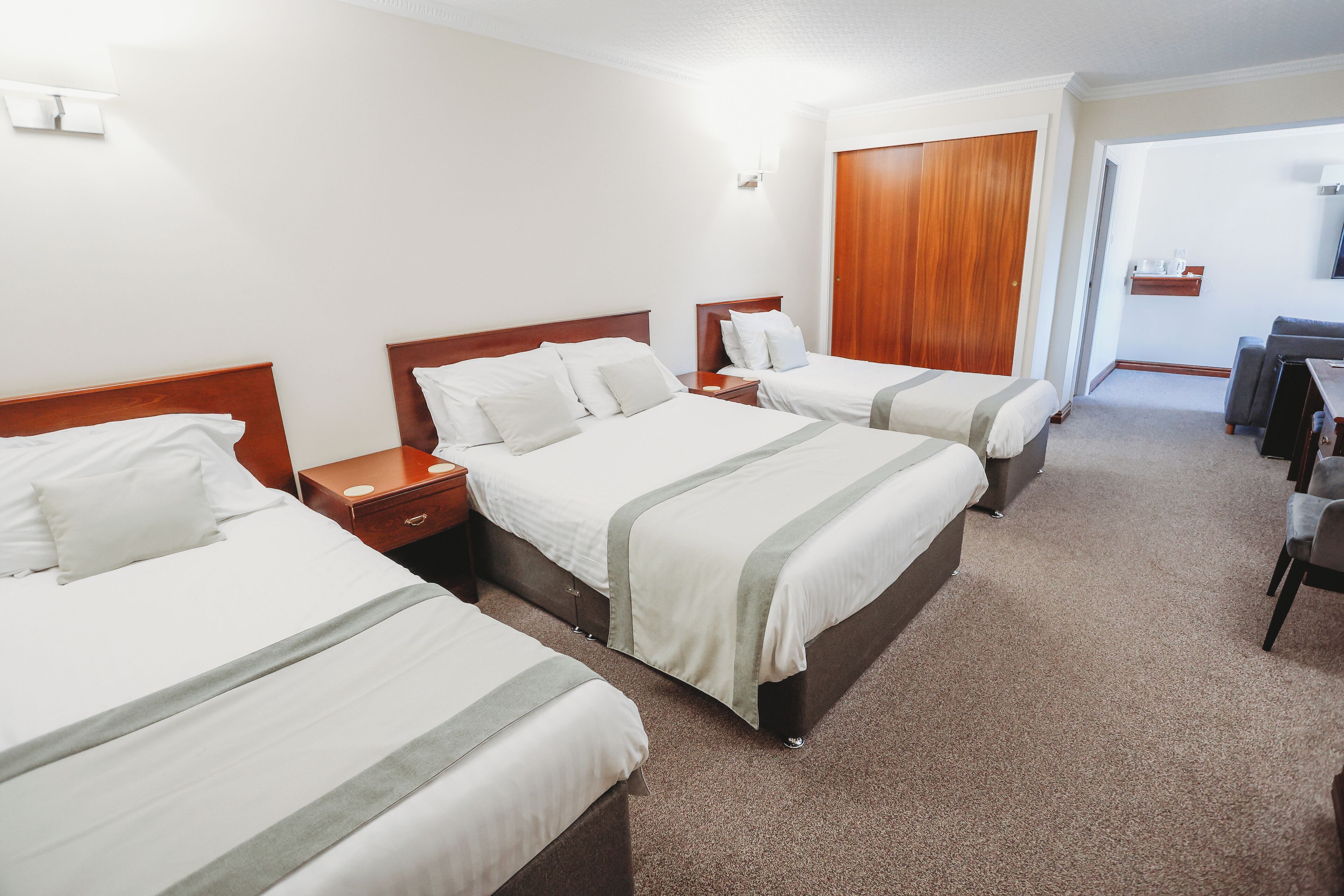 A hotel room with three beds, a wooden wardrobe, a desk, and a chair.