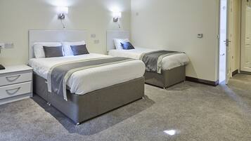 A hotel room with two beds, a nightstand, a dresser, and a door.