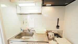 A compact kitchen with a stainless steel sink, a kettle, a white countertop, and a built-in oven.
