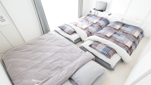 A modern hotel room with a large bed, two smaller beds, a TV, and a window.