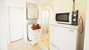 A compact kitchenette with a white refrigerator, a microwave, and a small sink with a drying rack.
