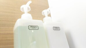 Two white bottles with labels, one labeled 'Shampoo' and the other 'Conditioner', placed on a wooden surface.