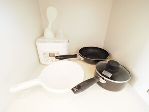 A kitchen area with a rice cooker, a frying pan, a spatula, and a pot.