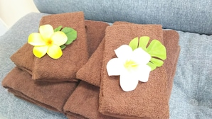 Ein Stapel brauner Handtücher mit künstlichen Blumen auf einem grauen Sofa.