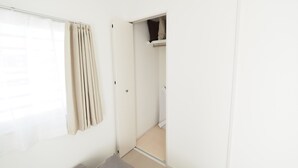 Ein Zimmer mit einem Bett, einem Vorhangfenster, einer Tür zu einem Schrank und einem Spiegel, der einen Teil des Raumes reflektiert.