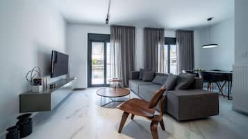 Una sala de estar moderna con un sofá, una silla de madera, un televisor y un comedor con mesa y sillas.