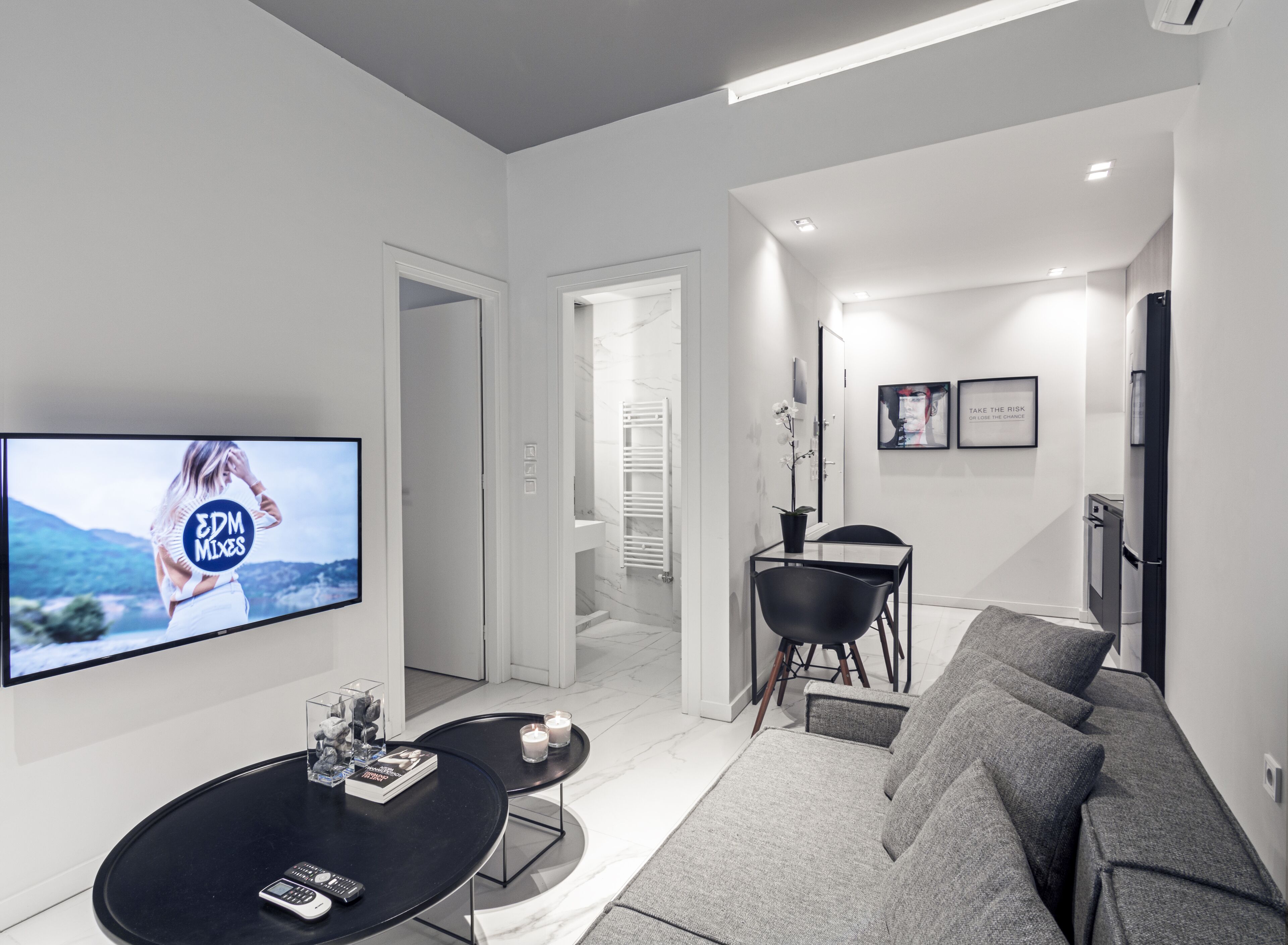 A modern living room with a flat-screen TV, a sofa, a coffee table, and a dining area with a chair and a small table.