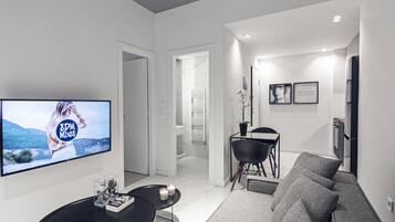 A modern living room with a flat-screen TV, a sofa, a coffee table, and a dining area with a chair and a small table.
