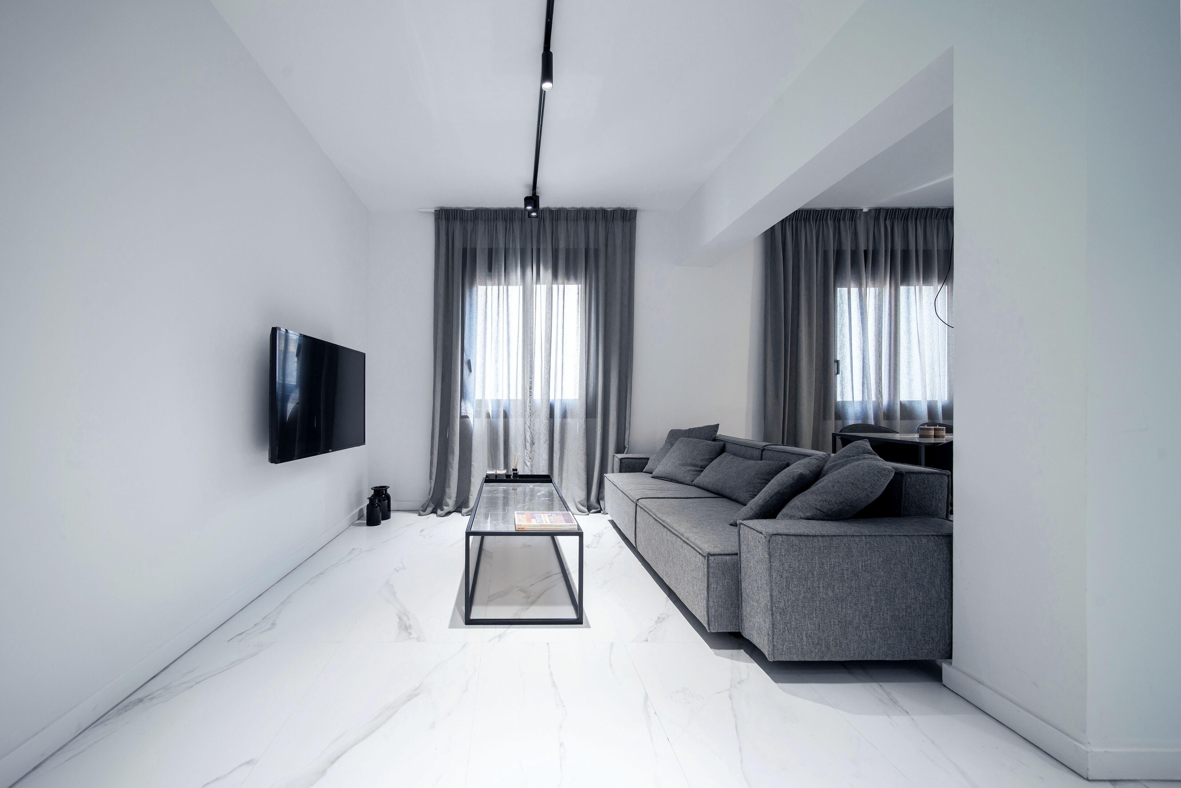 A modern living room with a flat-screen TV, grey sofa, and a glass coffee table.