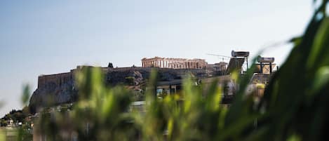 Um edifício histórico com colunas, uma muralha fortificada e uma estrutura moderna em primeiro plano.