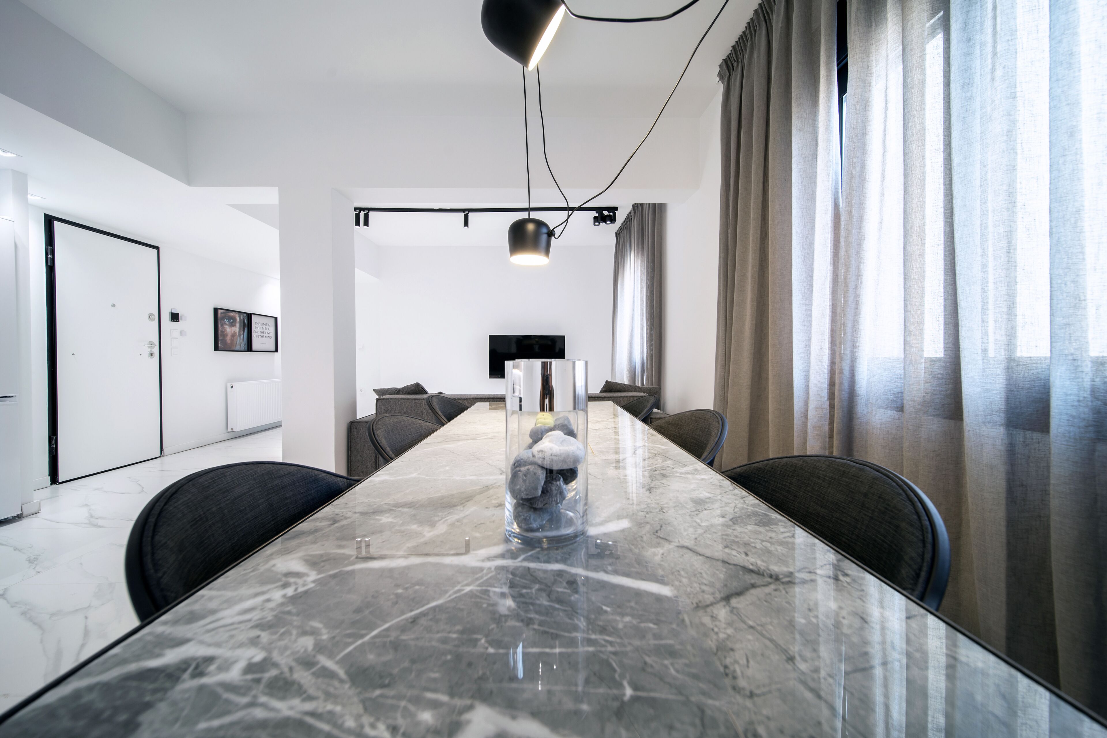 A modern conference room with a marble table, black chairs, a glass vase with stones, and a pendant light.