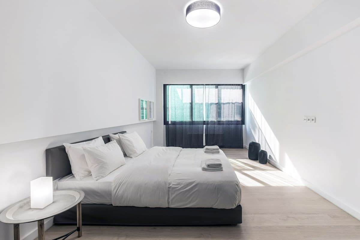 Quarto moderno com cama, mesa de cabeceira e uma janela grande.