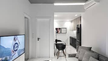 Un salon moderne doté d’un téléviseur à écran plat, d’un canapé, d’une table basse et d’un coin repas comprenant une chaise et une petite table.