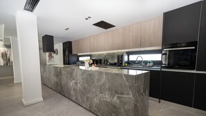 Una cocina moderna con una isla de mármol, armarios negros y electrodomésticos integrados.