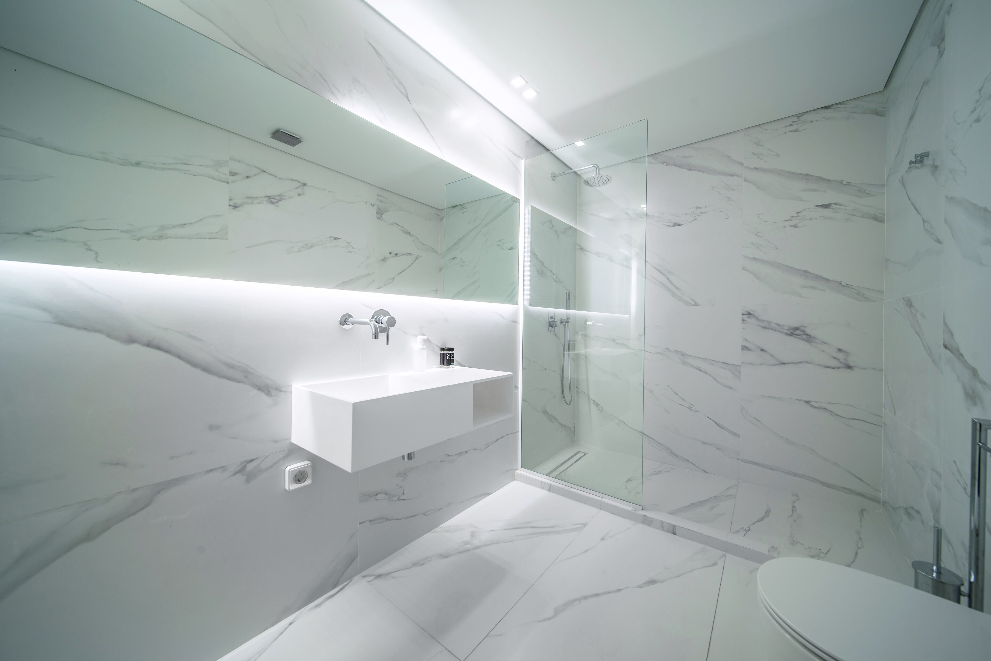 A modern bathroom with a marble backsplash, a glass-enclosed shower, and a white sink.