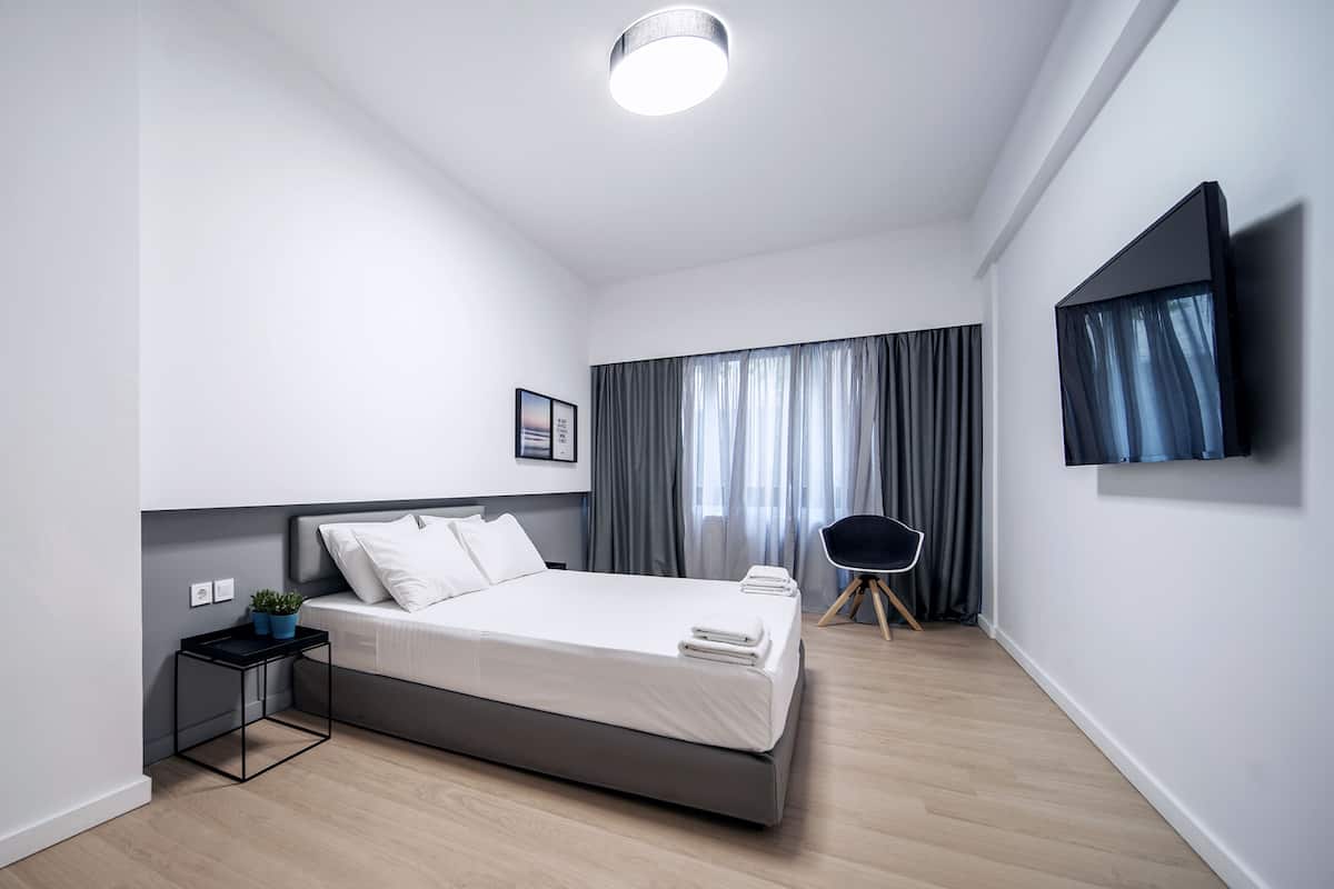 Quarto moderno com cama, mesa de cabeceira, televisão e cortinas.