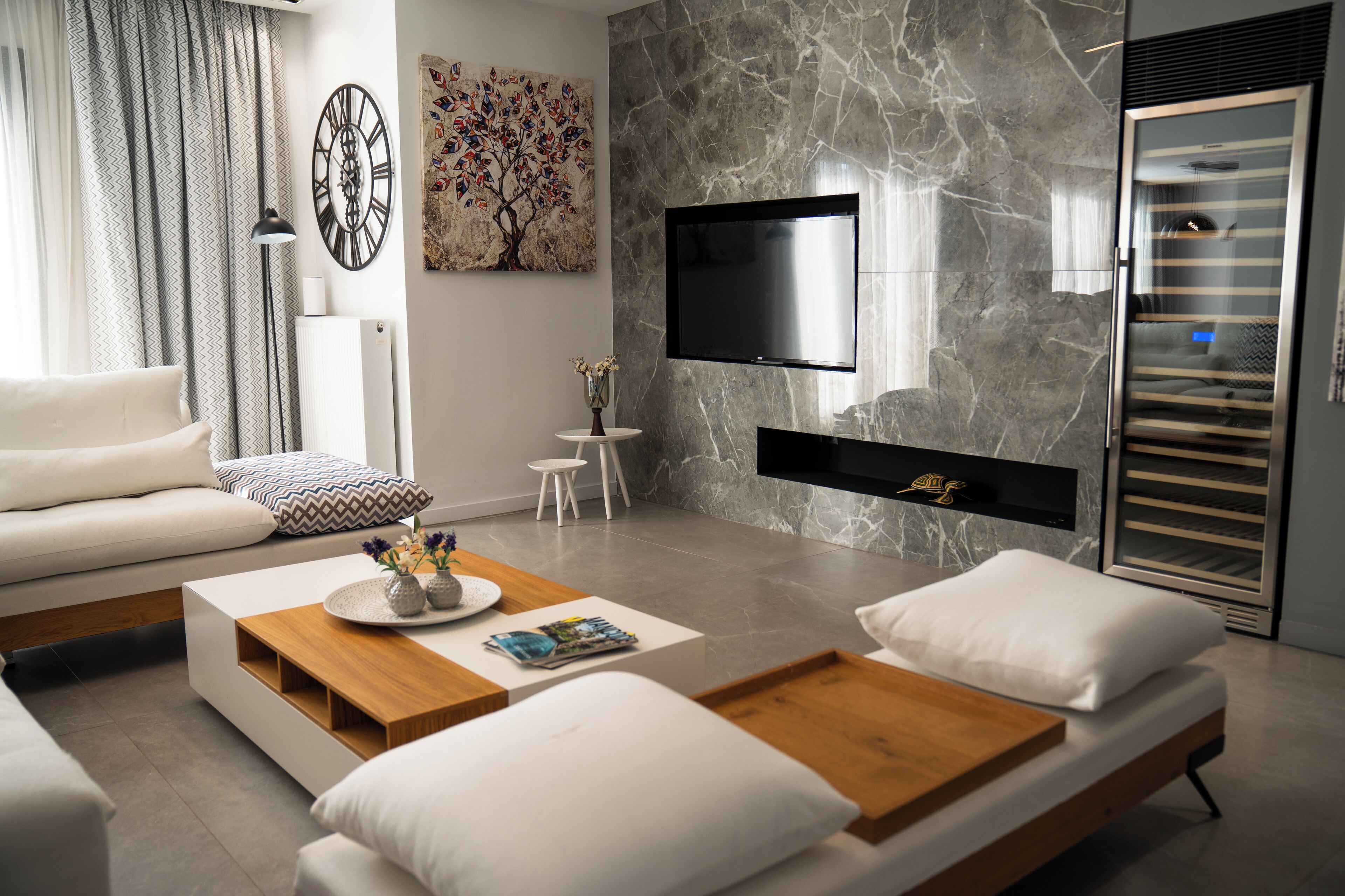 A modern living room with a sofa, coffee table, and a flat-screen TV mounted on a marble wall.