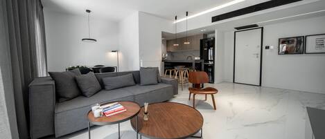 A modern living room with a grey sofa, two coffee tables, and a kitchen in the background.