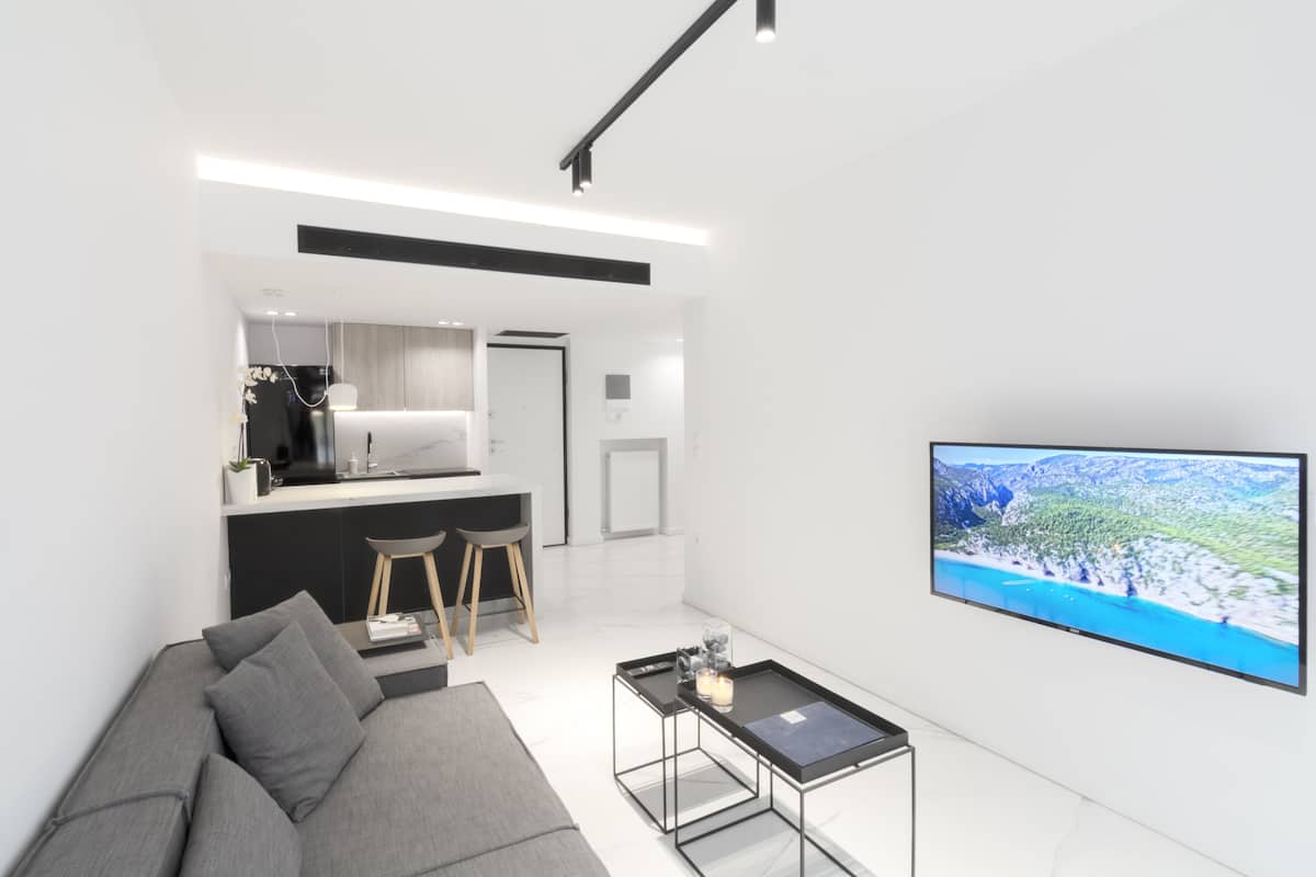 Uma sala de estar moderna com um sofá cinzento, uma mesa de centro pequena e uma TV de tela plana na parede.