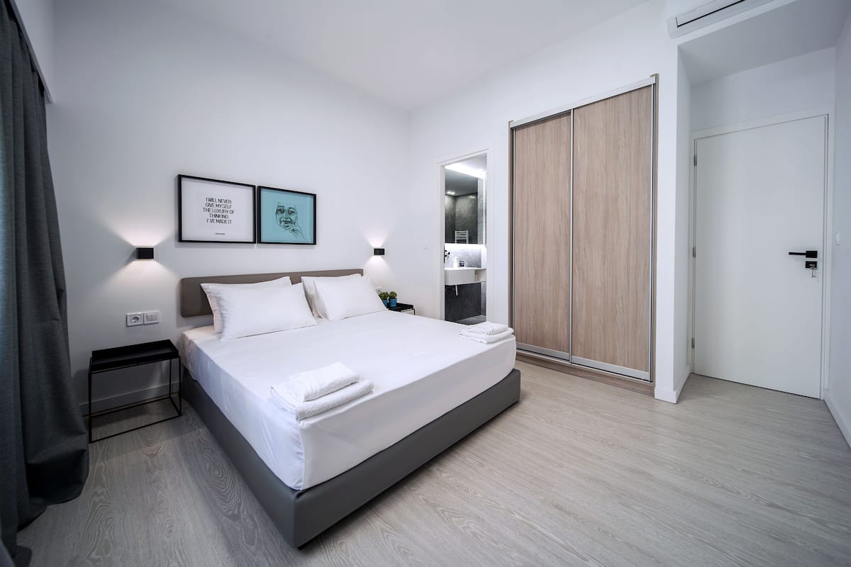 Quarto moderno com cama grande, mesas de cabeceira, guarda-roupa e quadros nas paredes.