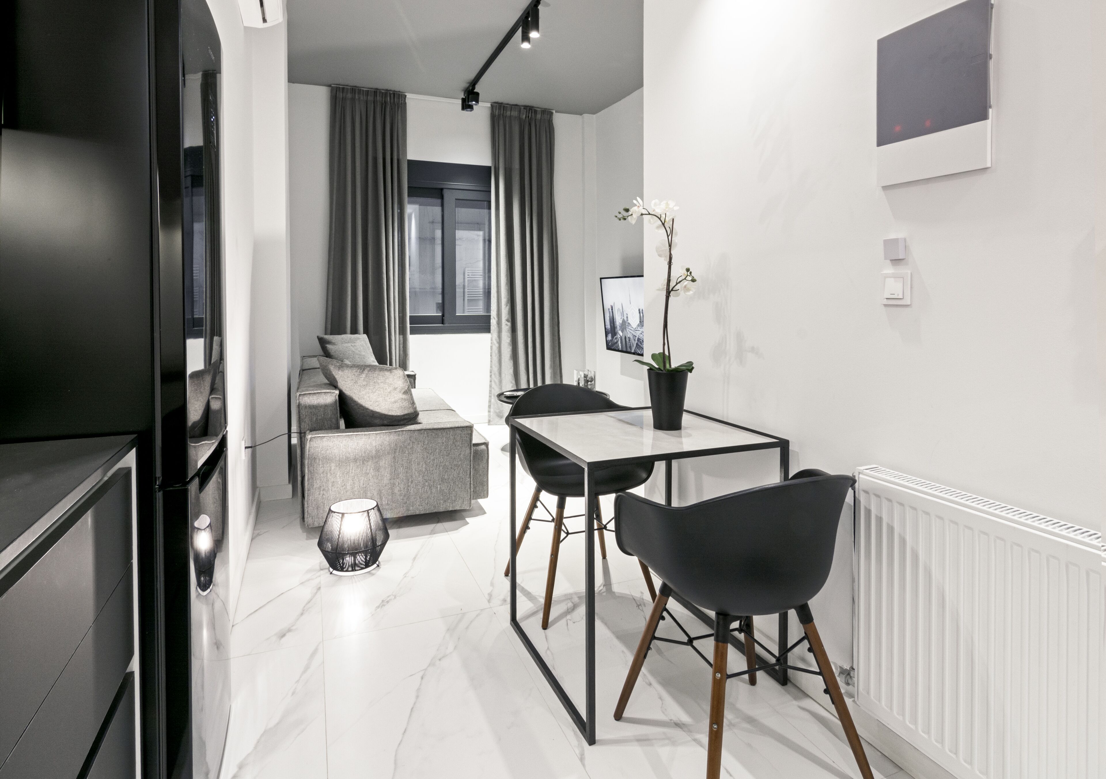 A modern, well-lit room with a dining table, chairs, a sofa, and a potted orchid.
