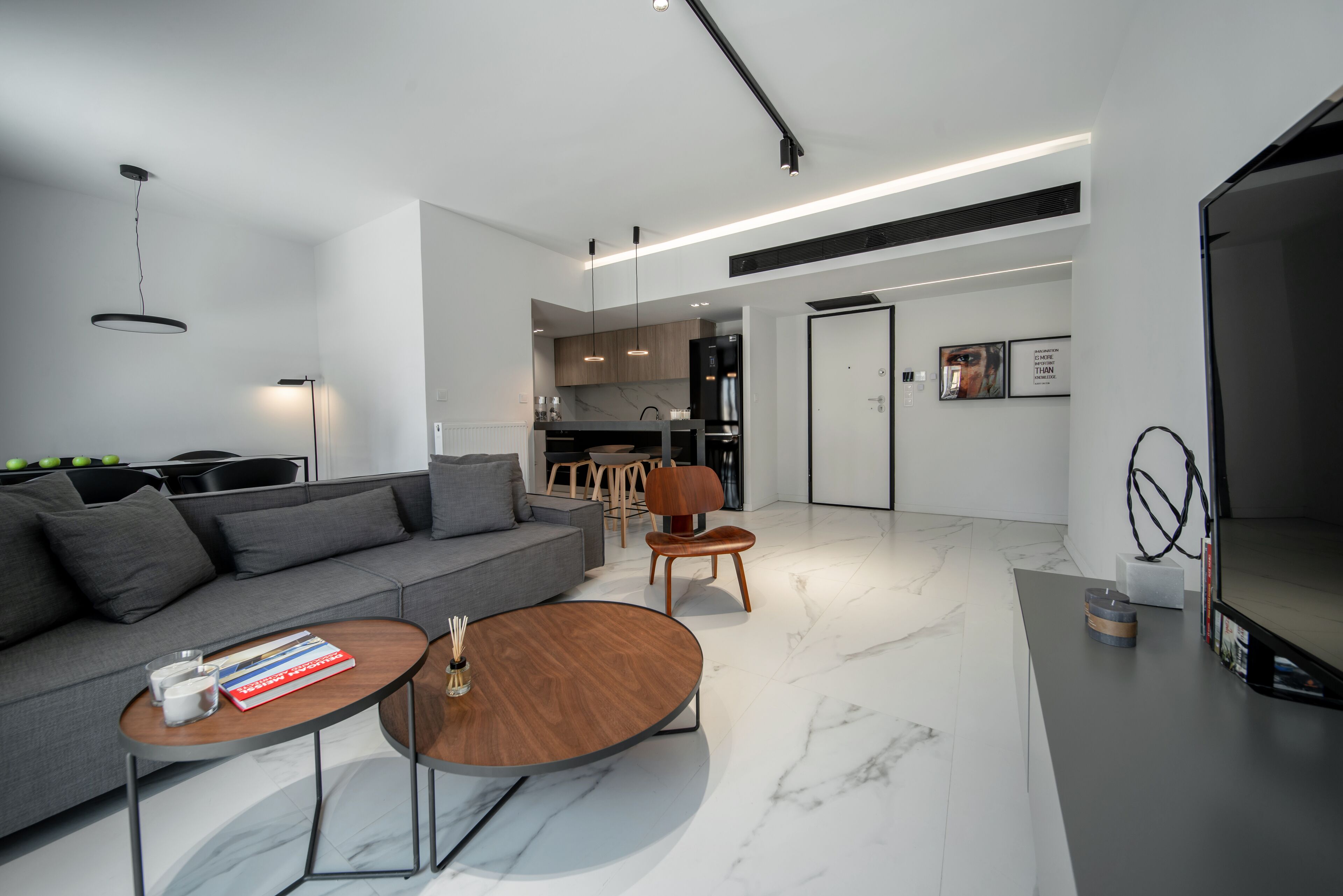 A modern living room with a grey sofa, wooden coffee table, and a dining area with a wooden chair.